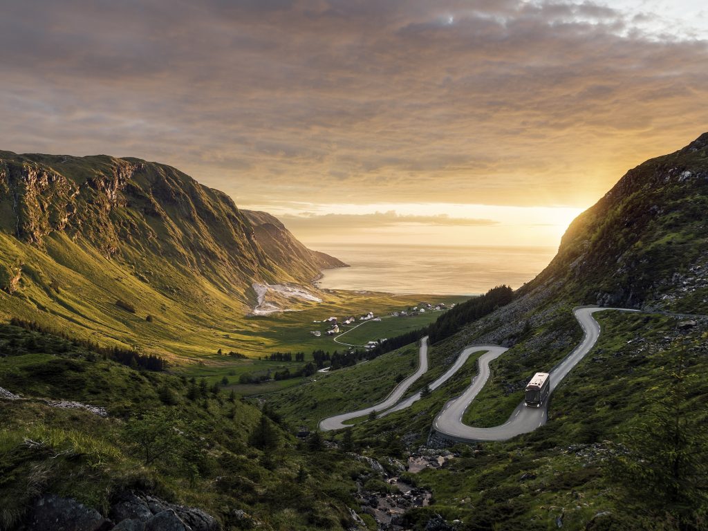 En Volvobuss som kör nedför en serpentinväg i en norsk fjord.