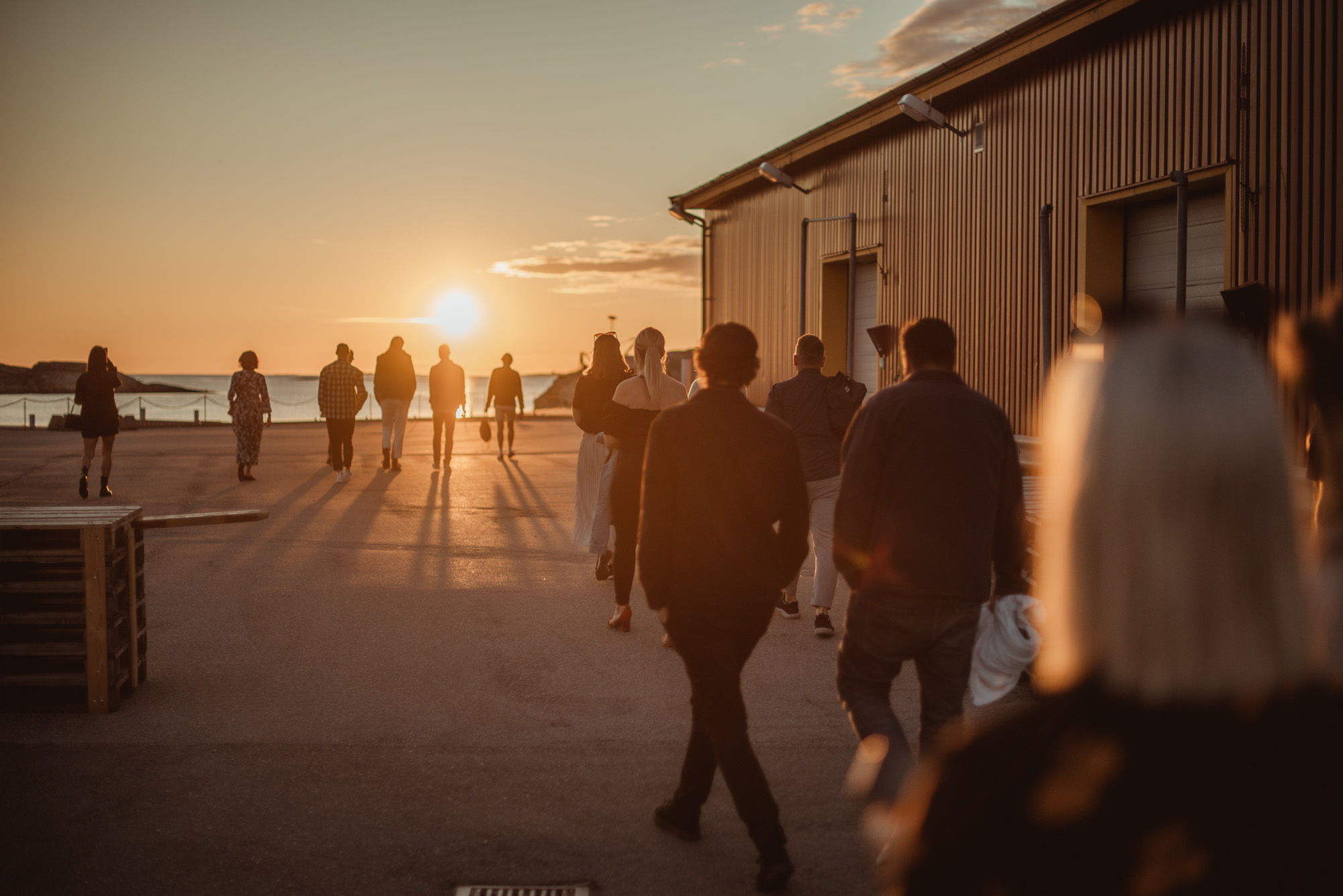 Människor på fest går på en brygga mot solen som går ner